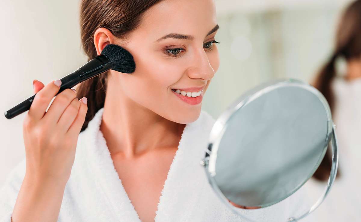 Donna che applica il blush davanti allo specchio per completare un make-up naturale e veloce in 5 passaggi