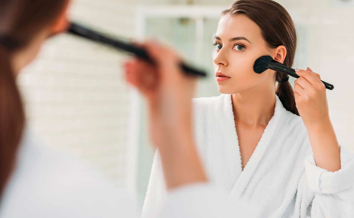 Donna riflessa allo specchio mentre applica il blush con un pennello per realizzare un make-up perfetto in pochi passaggi