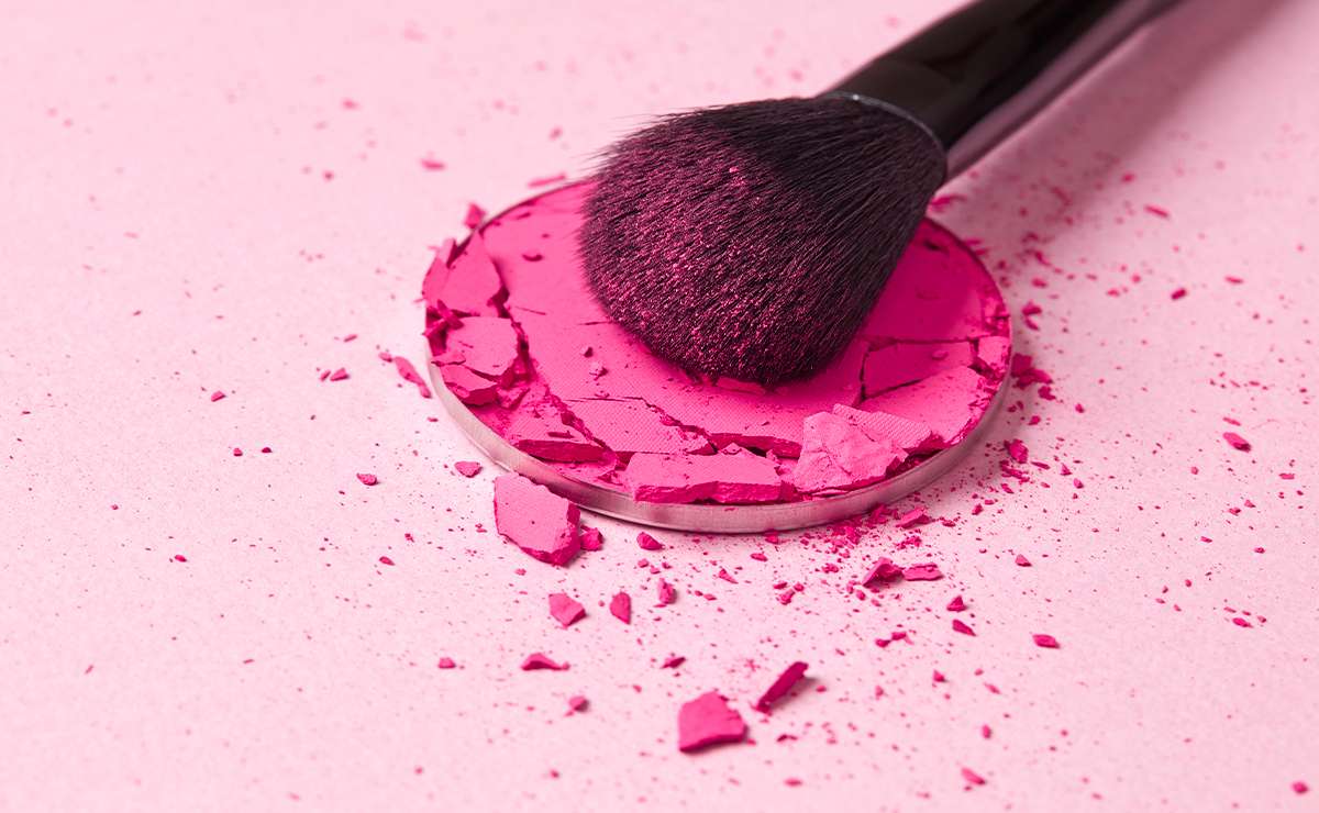 Pennello da trucco appoggiato su un blush rosa acceso frantumato