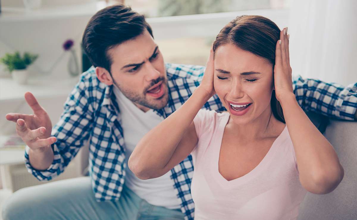 Coppia litiga sul divano in casa, lui urla e lei si tappa le orecchie disperata