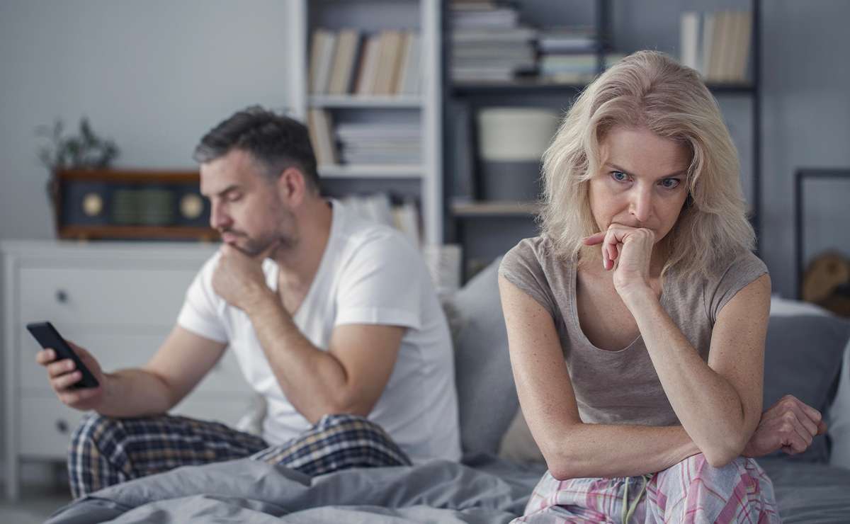 Uomo sullo sfondo guarda lo schermo del telefono, mentre la donna seduta accanto è infastidita