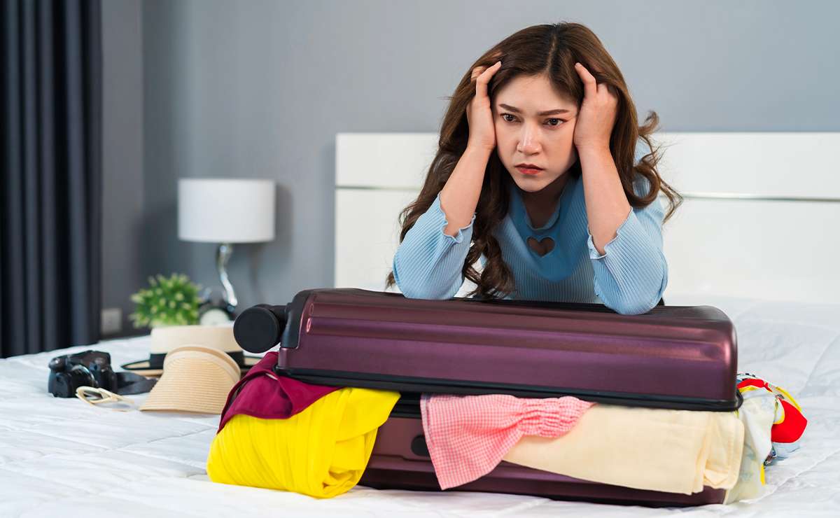 Donna frustrata mentre cerca di chiudere una valigia troppo piena, simbolo degli errori comuni da evitare quando si prepara la valigia per le vacanze.