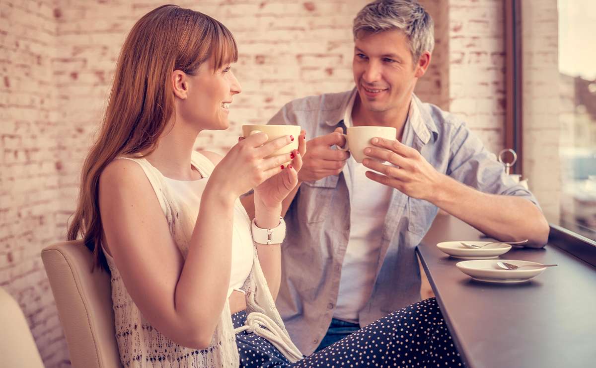 Coppia al primo appuntamento in un bar, sorride mentre beve caffè seduta vicino alla finestra