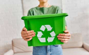 Persona che tiene in mano un contenitore verde per la raccolta differenziata con simbolo del riciclo, concetto di azioni sostenibili quotidiane