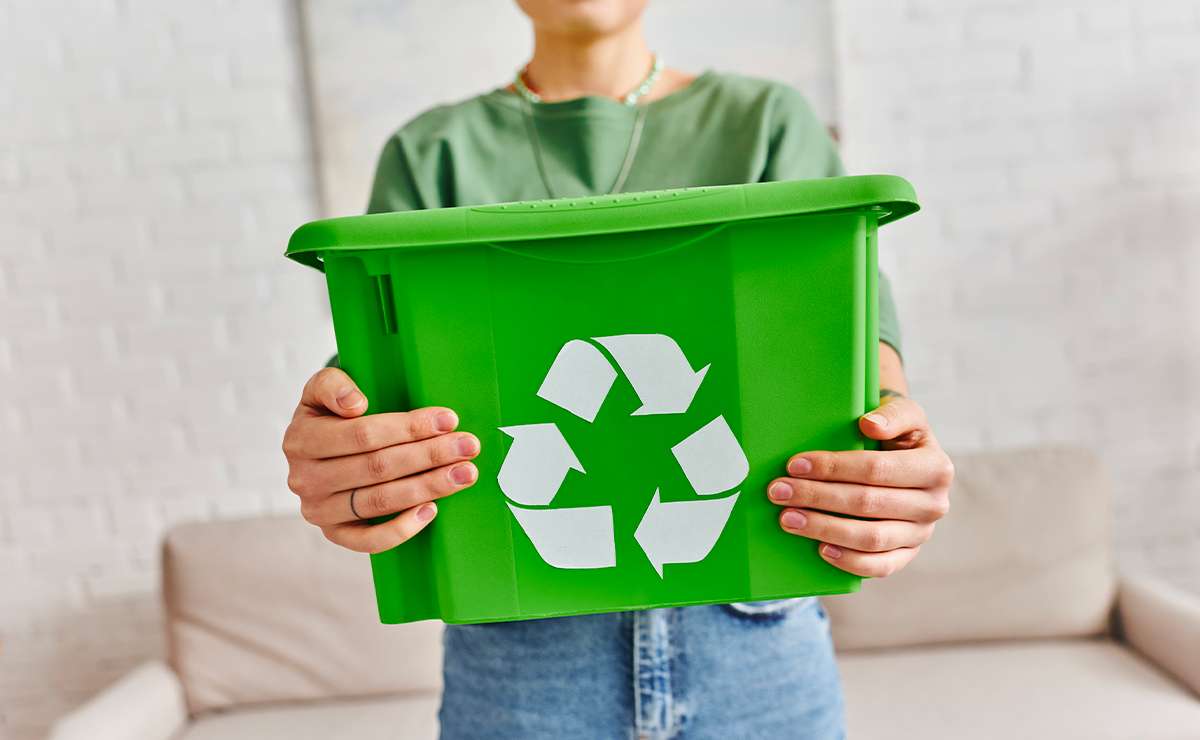 Persona che tiene in mano un contenitore verde per la raccolta differenziata con simbolo del riciclo, concetto di azioni sostenibili quotidiane