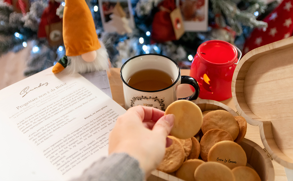 Piparkökur, biscotti speziati in scatola di legno accanto a una tazza da tè con un albero di natale sullo sfondo
