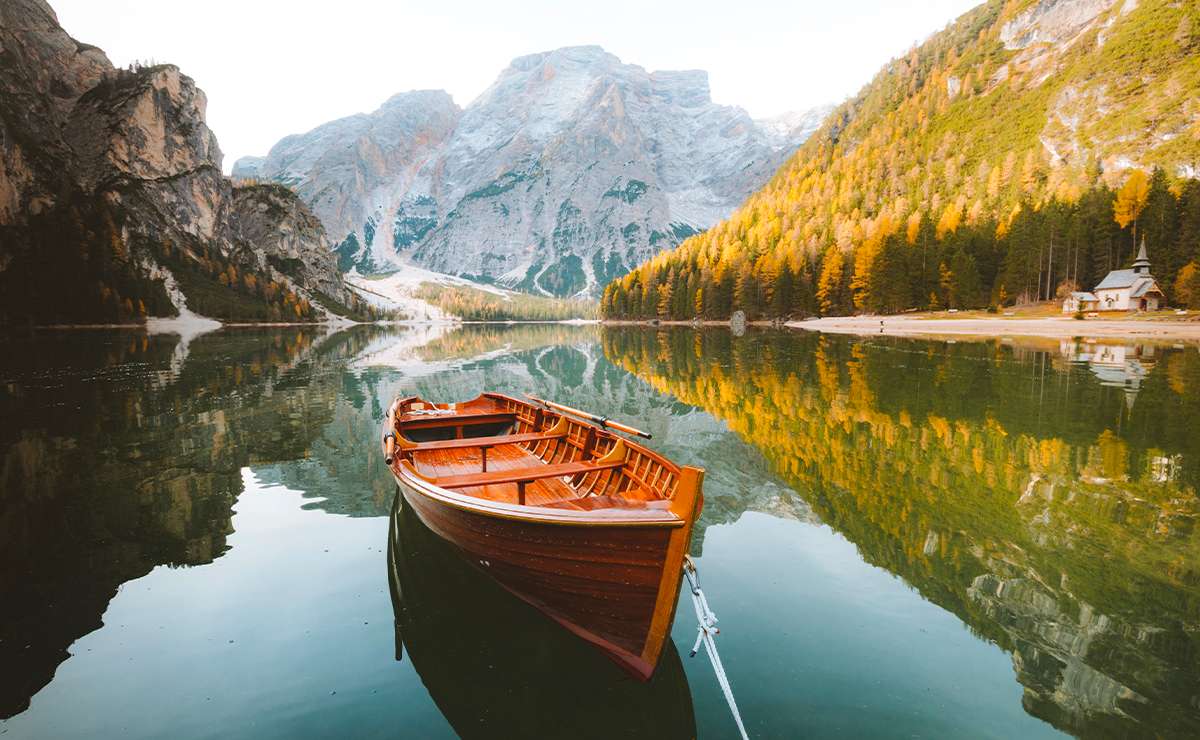 Barca in legno sul Lago di Braies circondata da alberi autunnali e montagne riflettenti sull’acqua, meta perfetta per il foliage in Italia.