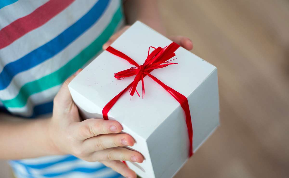 Bambino che regge un pacco regalo bianco con fiocco rosso, simbolo dei regali di Natale per le maestre scelti con affetto e semplicità.