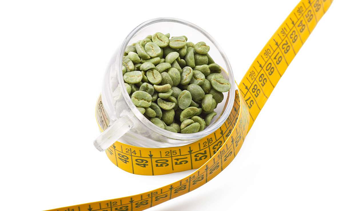 Tazza di vetro piena di chicchi di caffè verde avvolta da un metro da sarta giallo, simbolo del legame tra caffè verde e dimagrimento.