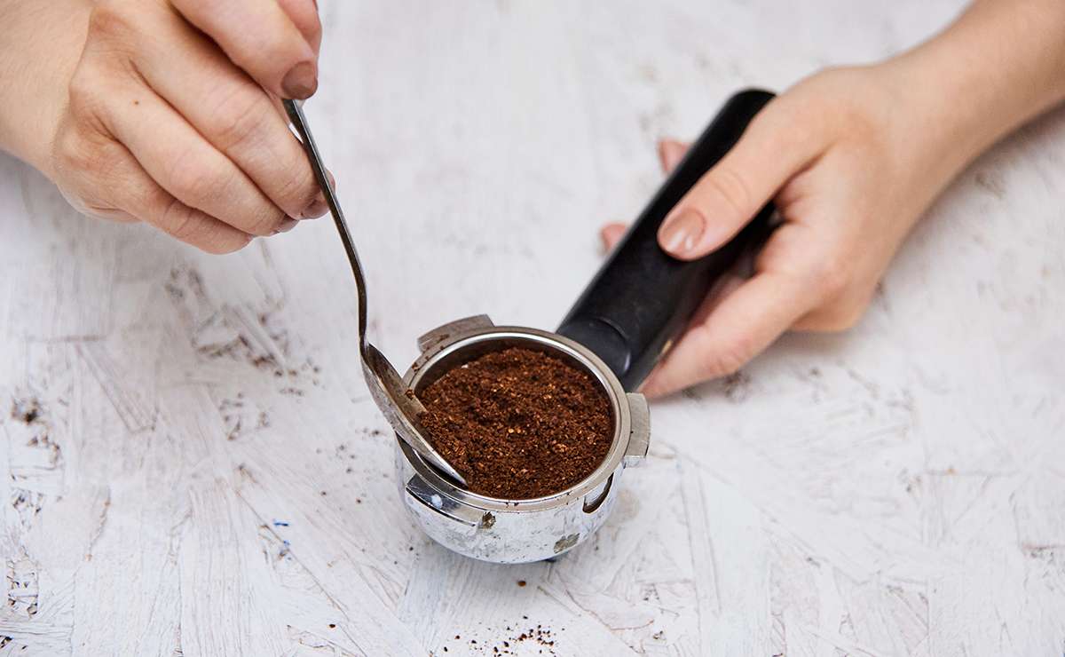 Mani che utilizzano un cucchiaino per raccogliere i fondi di caffè dal portafiltro di una macchina da caffè
