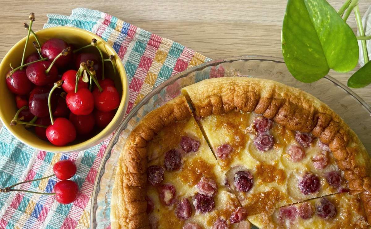 clafoutis di ciliegie su tovaglietta a scacchi colorati e accanto una ciotola di ciliegie fresche