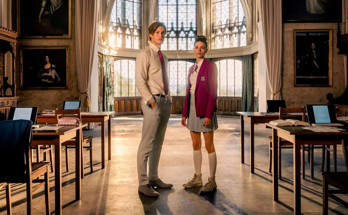 Immagine tratta dalla serie tv Maxton Hall, i due protagonisti James e Ruby in piedi nell'aula della prestigiosa scuola.