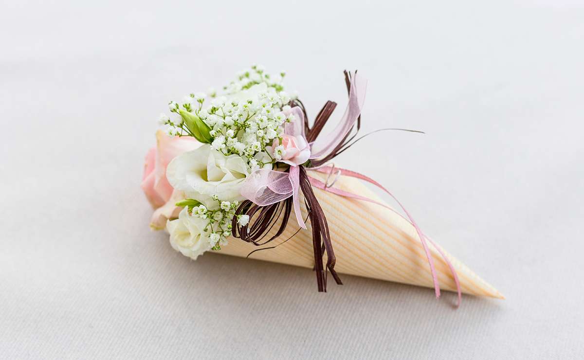 Cono portaconfetti decorativo realizzato in carta con motivo a righe delicate, ornato con nastri colorati e piccoli fiori bianchi e rosa. Perfetto per matrimoni o cerimonie eleganti.
