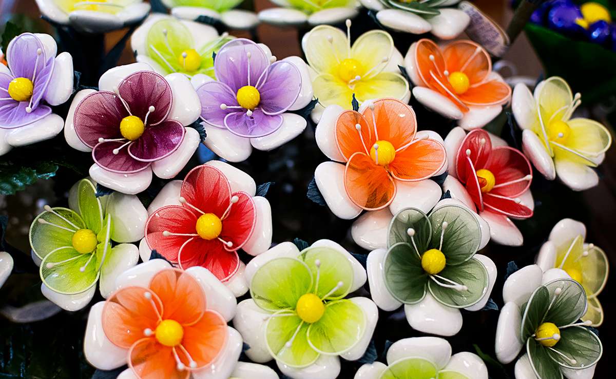Fiori di confetti di Sulmona realizzati a mano con petali colorati in tessuto di tulle rosso, arancione, viola, verde e giallo, assemblati con confetti bianchi triangolari e al centro un confetto a pallina giallo come decorazione artigianale.