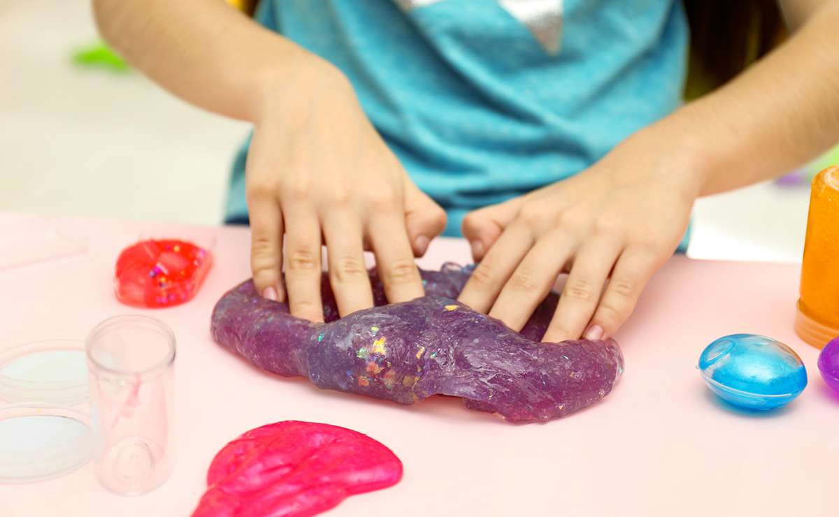 Bambino che gioca con slime colorato su un tavolo, circondato da contenitori trasparenti e altri slime colorati.