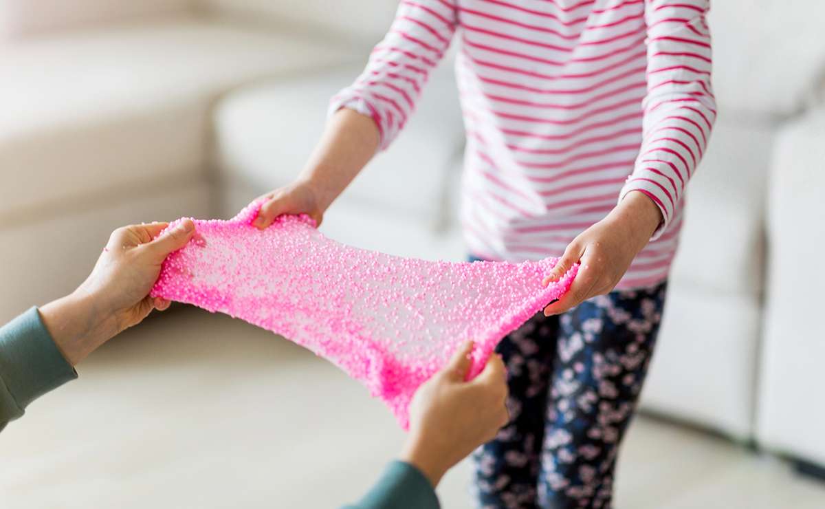 Due persone che giocano insieme tirando uno fluffly slime rosa con perle, in un ambiente domestico luminoso e accogliente.