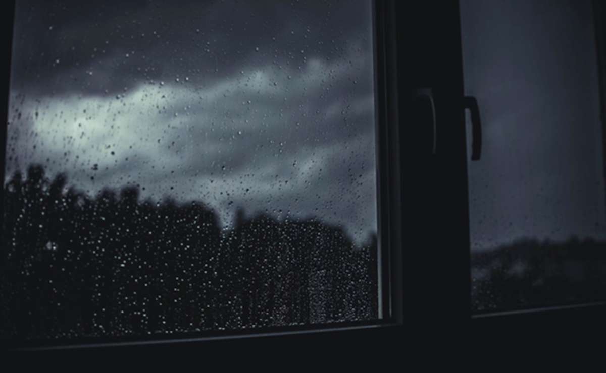 Finestra con vetro bagnato dalla pioggia e cielo scuro, ideale per ispirare idee e attività da fare durante una giornata di pioggia.