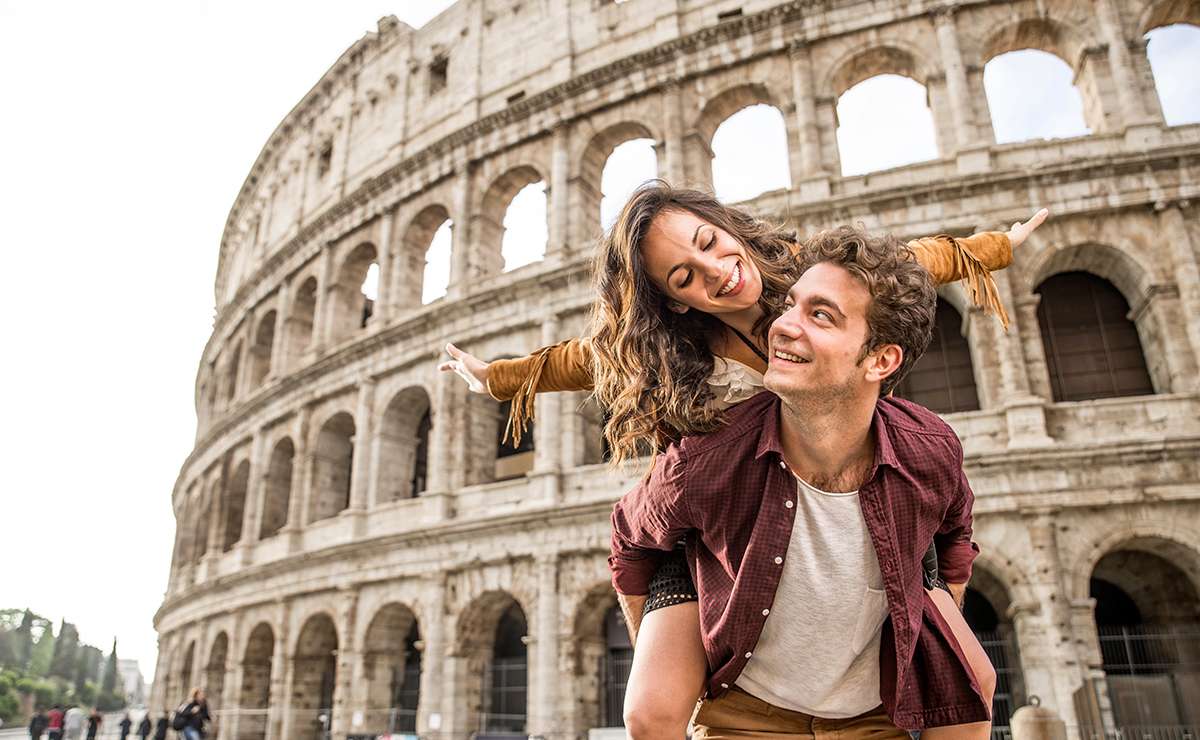 Coppia sorridente davanti al Colosseo a Roma, simbolo di una giornata romantica trascorsa tra le meraviglie storiche e artistiche delle città d'arte italiane per San Valentino.