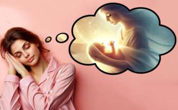 Una donna addormentata con un'espressione serena indossa un pigiama rosa. Sopra di lei appare un'illustrazione onirica in una nuvola di pensiero, raffigurante una figura femminile che tiene in braccio un neonato avvolto in una luce calda e soffusa, simbolo di sogno e rinascita.