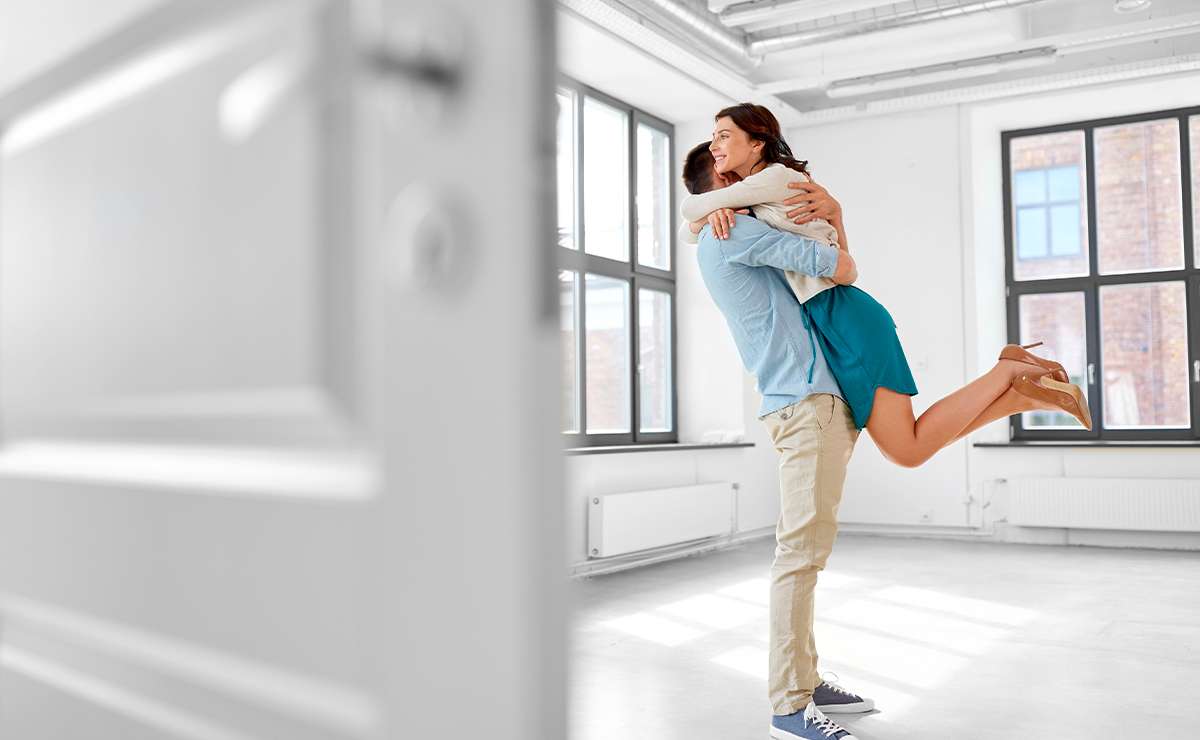 Coppia felice che si abbraccia in una casa con grandi finestre, simbolo di un ambiente confortevole e sicuro grazie a infissi su misura.