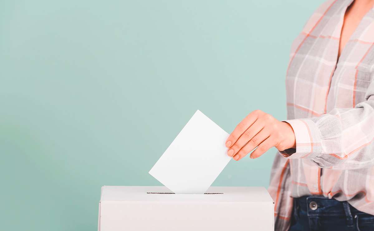 Primo piano di una donna che inserisce una scheda bianca in un’urna elettorale, simbolo del diritto di voto femminile e della partecipazione democratica.