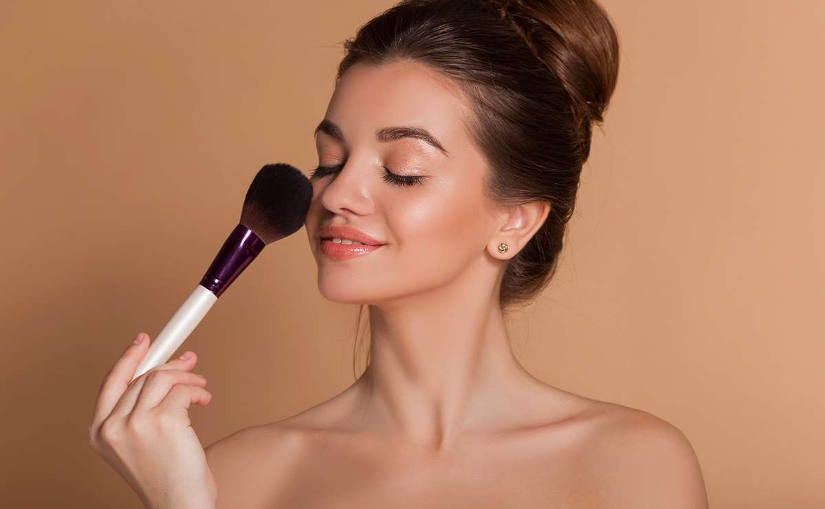 Donna con make-up naturale estivo applica il blush con un pennello, pelle luminosa e trucco leggero a prova di caldo