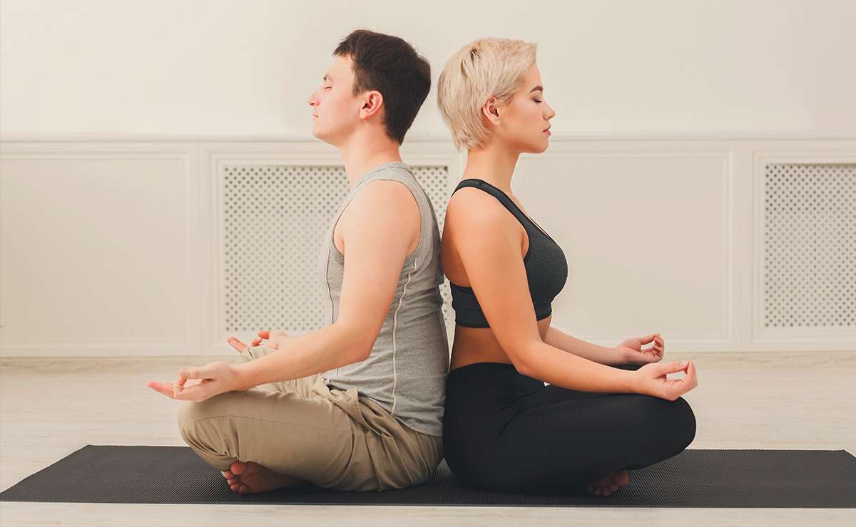 Uomo e donna seduti schiena contro schiena su un tappetino da yoga mentre praticano la meditazione, tecnica utile per stimolare ed equilibrare il nervo vago.