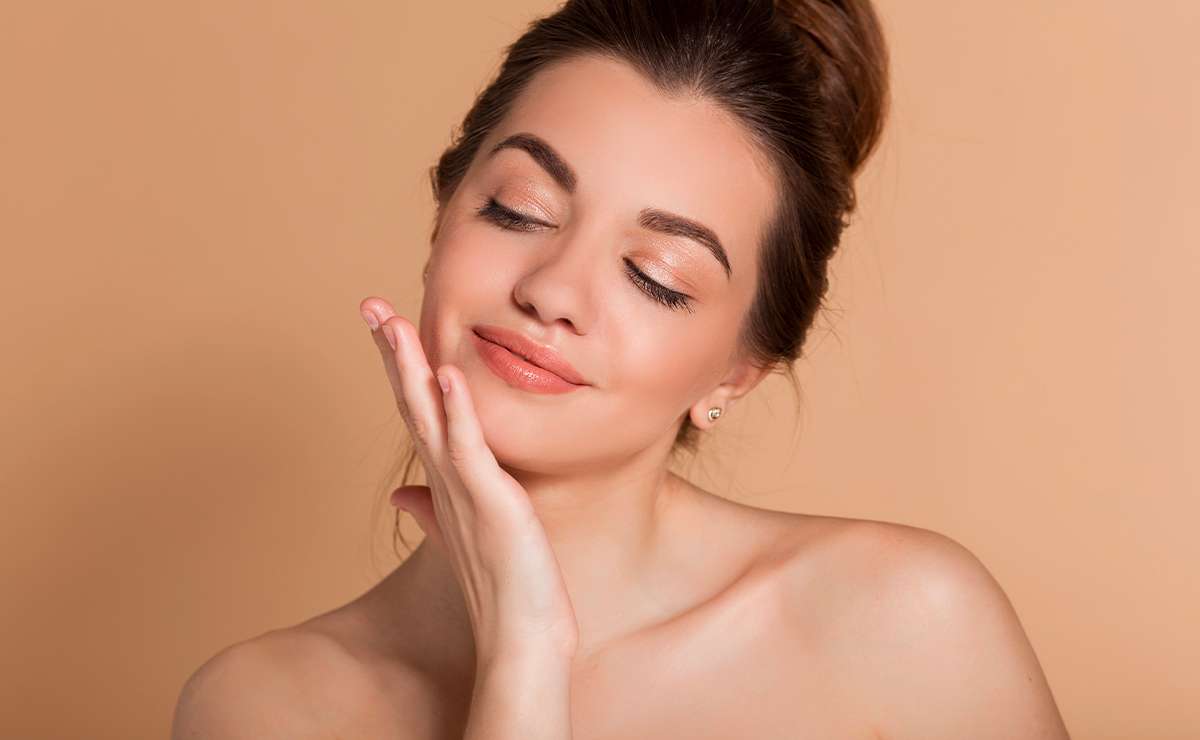 Donna con trucco naturale estivo tocca il viso truccato con ombretti nude e finish luminoso, ideale per un look fresco e leggero