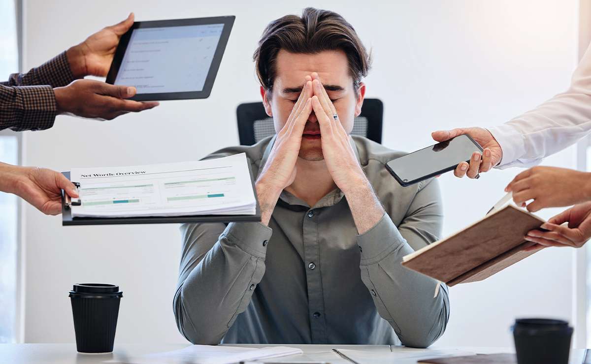 Uomo stressato alla scrivania sommerso da richieste di lavoro, simbolo di ambiente lavorativo tossico