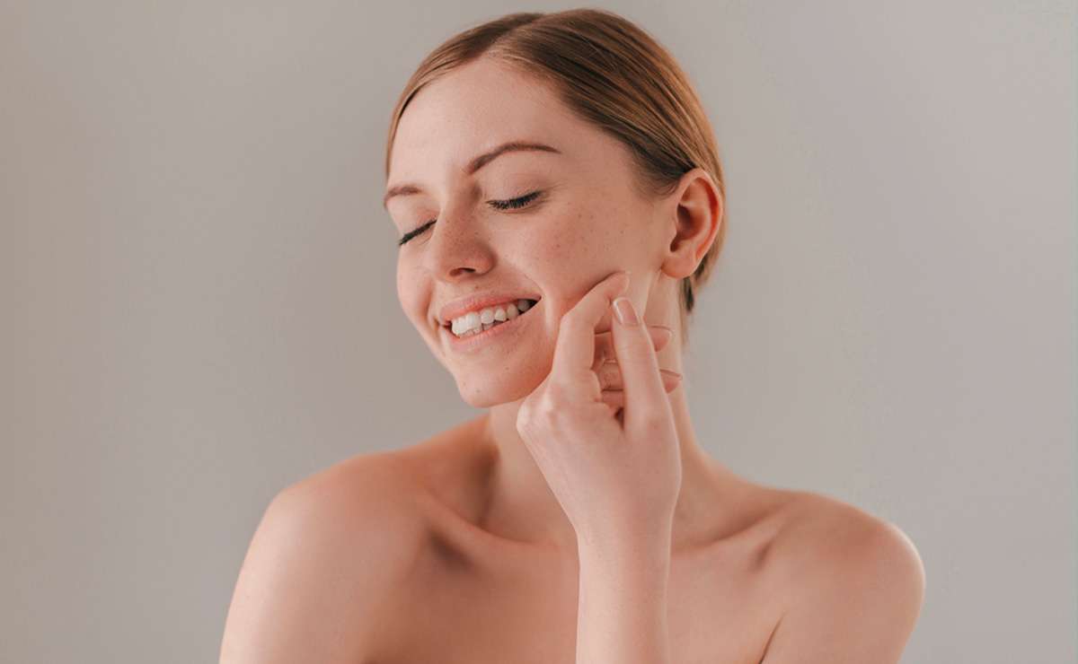 Donna con pelle liscia che sorride accarezzandosi il viso