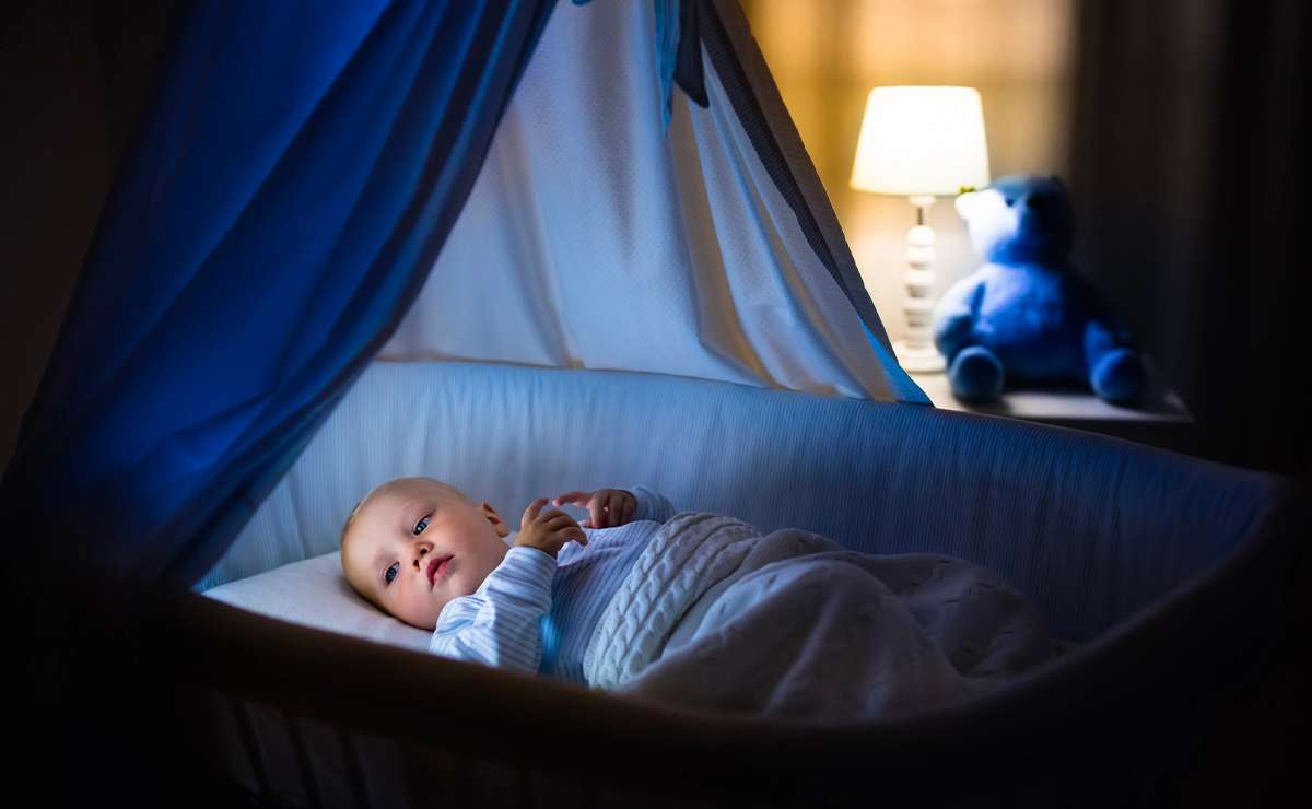 Neonato sveglio nella culla di notte con luce soffusa e atmosfera tranquilla