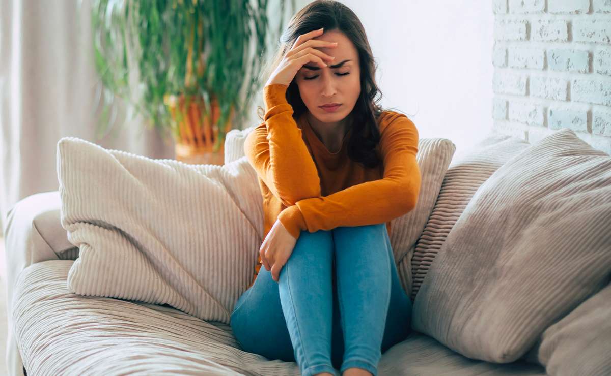 Donna seduta sul divano con espressione sofferente, mano sulla fronte e occhi chiusi, simbolo del dolore emotivo dopo una rottura sentimentale.