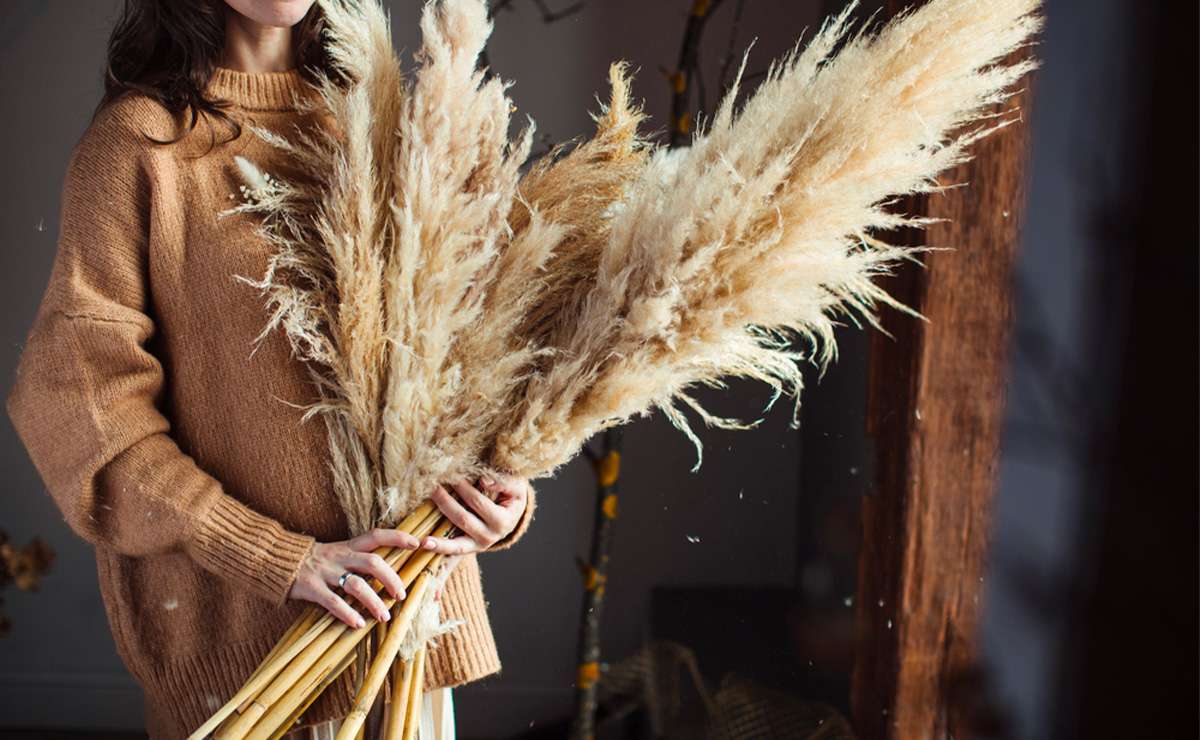 Donna con maglione marrone che tiene in mano un grande mazzo di pampas essiccato, ideale per decorazioni floreali in stile naturale e boho.