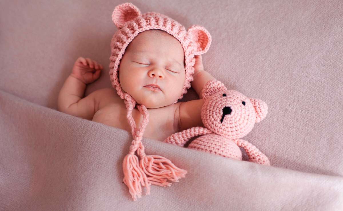 Neonata che dorme avvolta in una coperta rosa con cappellino a orecchie e orsetto di lana