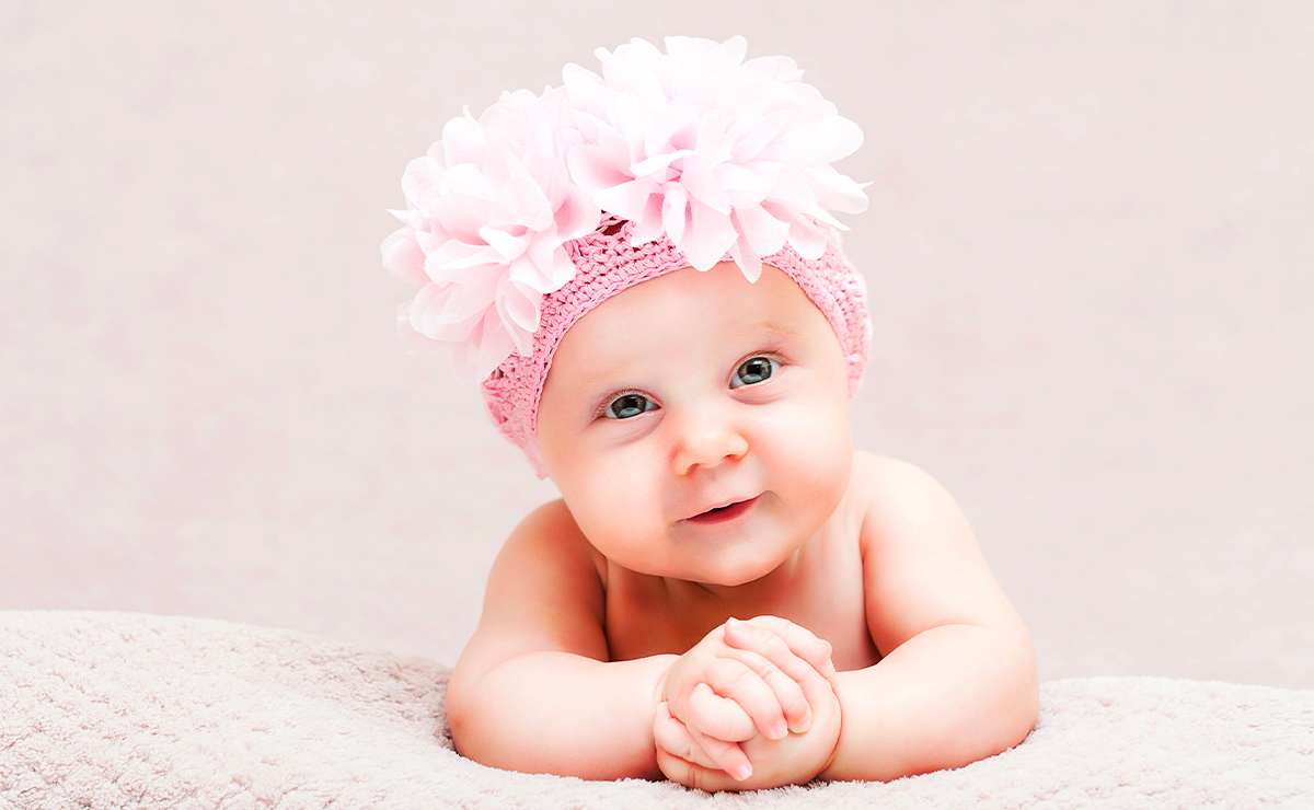 Neonata con fascia rosa decorata da grandi fiori, appoggiata su coperta chiara