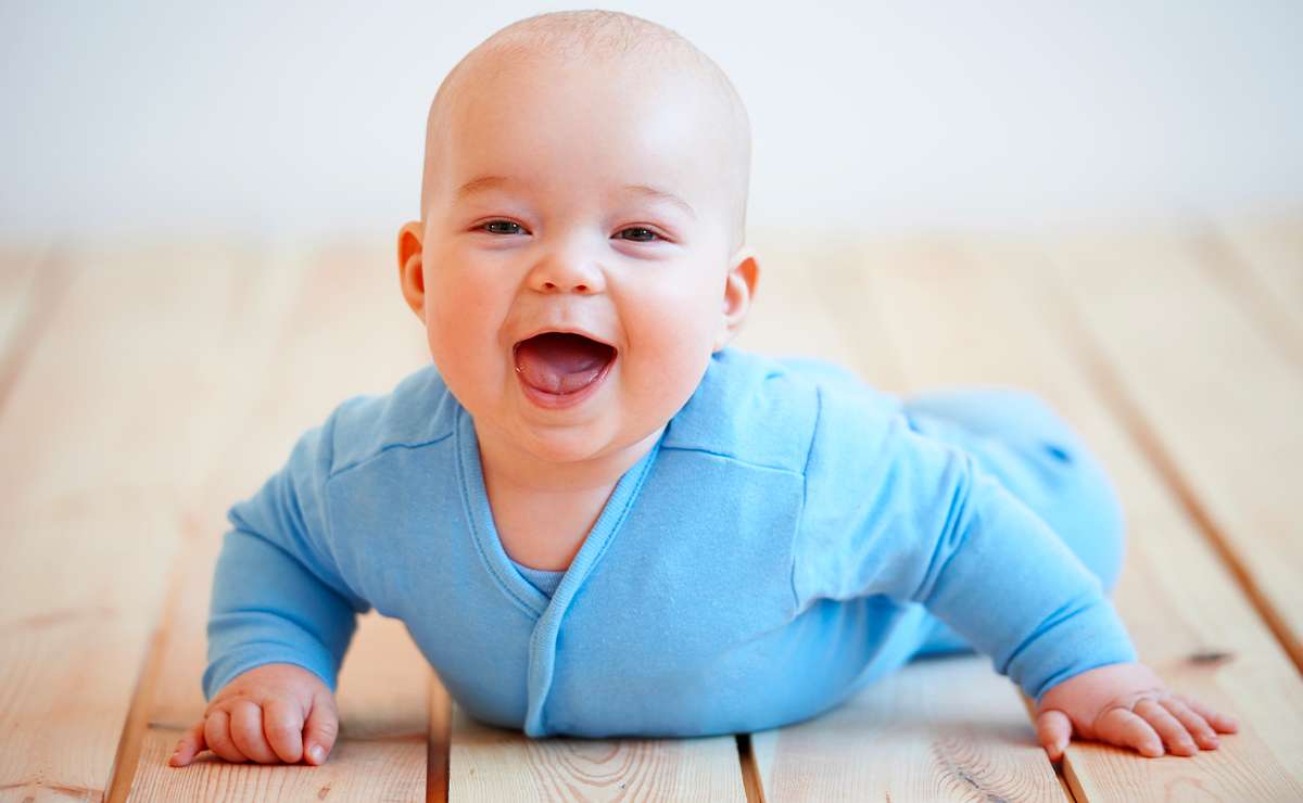 Bambino sorridente con tutina azzurra disteso sul pavimento