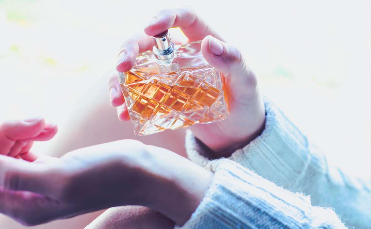 Donna che vaporizza un profumo sul polso, inquadratura ravvicinata su una bottiglia elegante con liquido ambrato