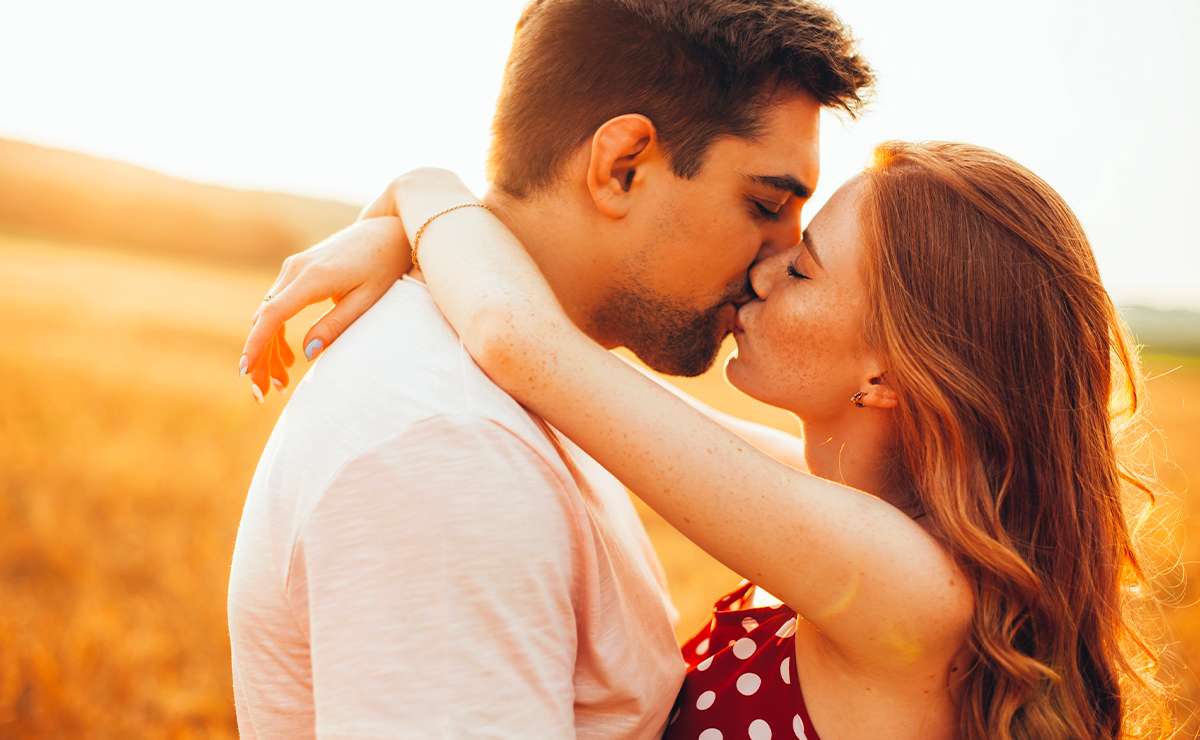 Coppia che si bacia al tramonto in un campo dorato, con atmosfera romantica e luce calda d’estate.