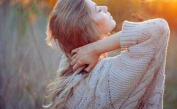 Donna bionda con occhi chiusi immersa nella natura al tramonto, espressione serena e contemplativa che trasmette sensibilità ed emozione.