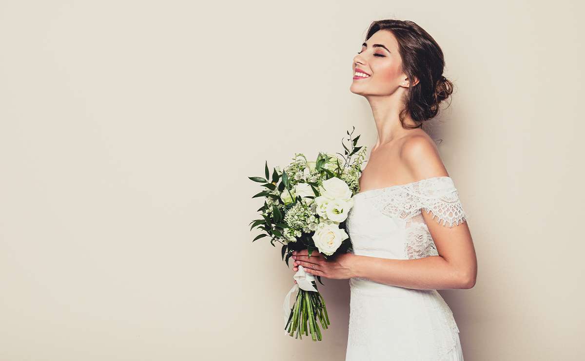 Sposa con abito in pizzo e bouquet bianco, sorridente e radiosa, in un momento intimo e felice prima del matrimonio.