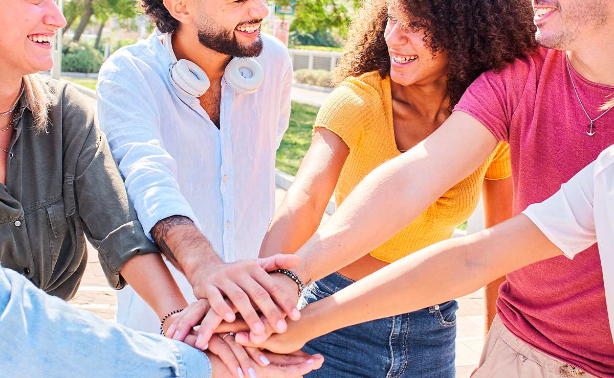 Gruppo di amici uniti con le mani sovrapposte che sorridono all’aperto, simbolo di amicizia vera, complicità e legame profondo