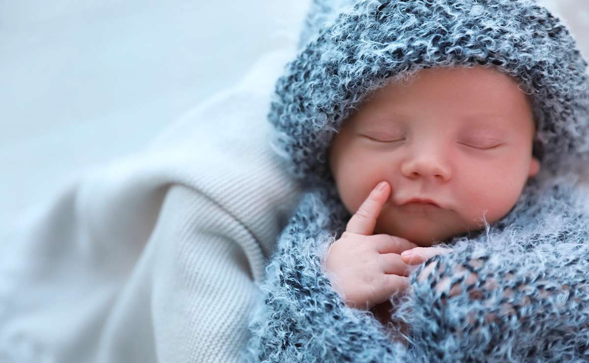 Neonato che dorme sereno, avvolto in una coperta blu e con un cappellino coordinato, primo piano dolce e ravvicinato.