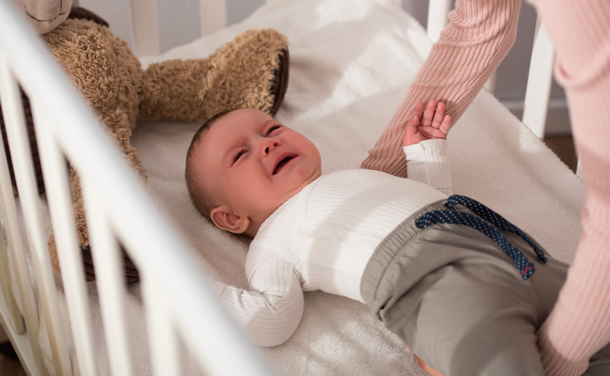 Neonato che piange nella culla durante il giorno, assistito da una figura adulta, possibile episodio di pianto inconsolabile o disagio notturno.