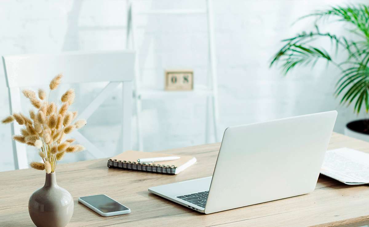 Scrivania ordinata in stile Feng Shui con laptop, pianta verde e luce naturale in un ambiente di lavoro minimal e rilassante