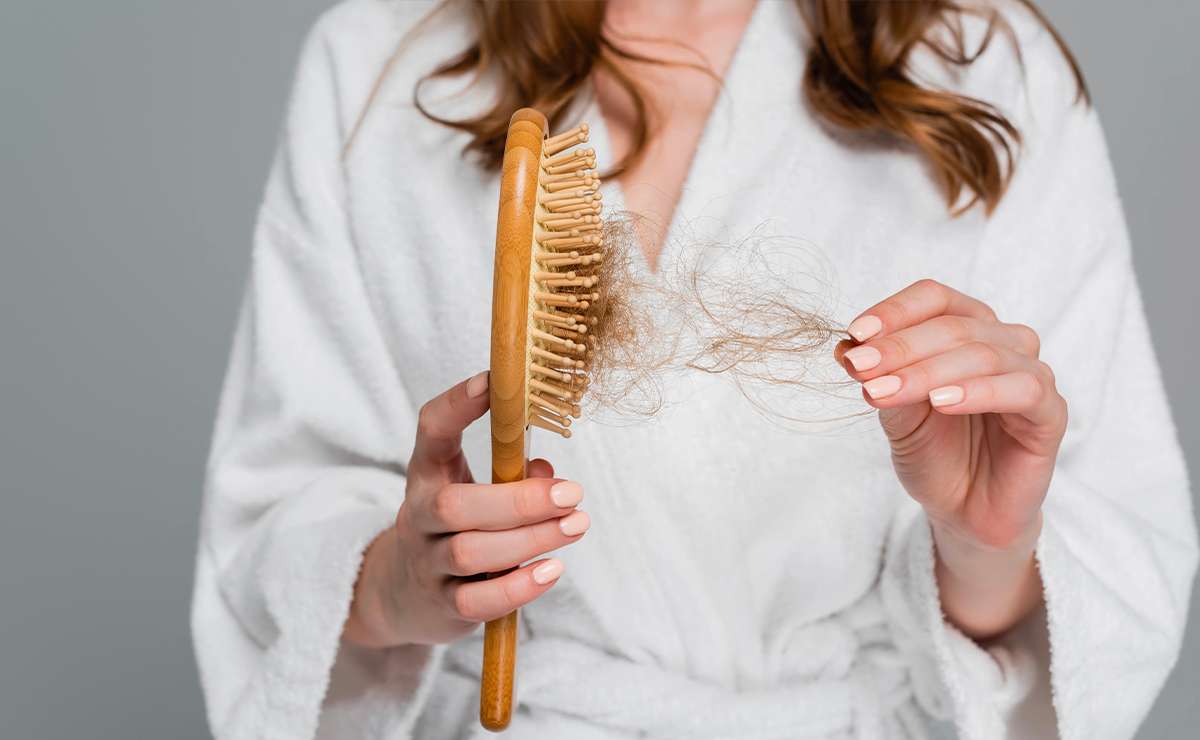 Donna in accappatoio tiene una spazzola con molti capelli persi: immagine simbolo della caduta dei capelli e delle sue possibili cause.