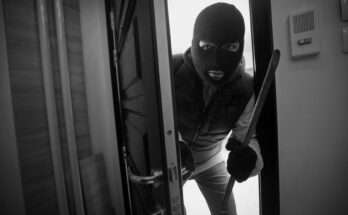 Ladro con passamontagna e piede di porco entra in un appartamento forzando la porta: immagine simbolo dei furti in casa durante le vacanze estive.