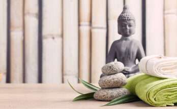 Composizione zen con statua di Buddha, pietre sovrapposte, asciugamani arrotolati e foglie verdi su sfondo in bambù, simbolo di armonia e Feng Shui