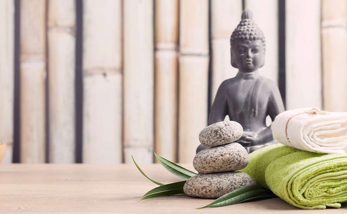 Composizione zen con statua di Buddha, pietre sovrapposte, asciugamani arrotolati e foglie verdi su sfondo in bambù, simbolo di armonia e Feng Shui