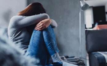 Donna seduta con le ginocchia al petto in un momento di profondo sconforto, simbolo visivo della sofferenza emotiva legata alla depressione