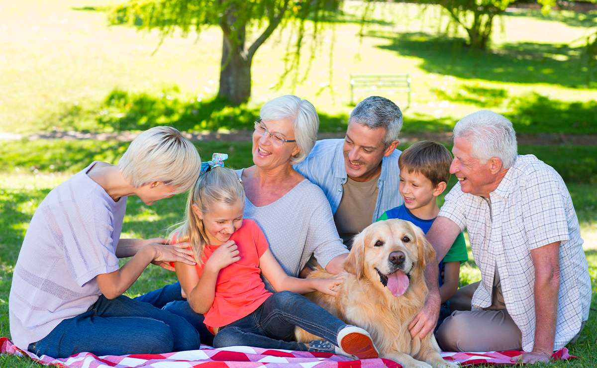Famiglia sorridente riunita all’aperto su una coperta con il loro cane Golden Retriever, simbolo dell’amore e dei legami familiari inclusivi.